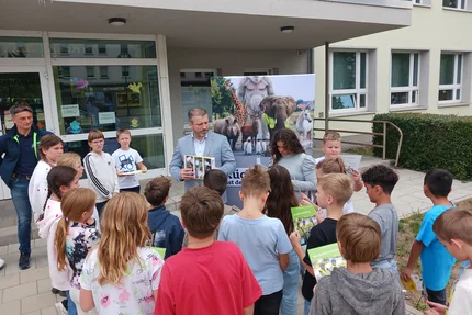Calbe Saale © AGFK LSA Ein Mann zeigt einer Schulklasse in Calbe das Heft „Die Radfahrausbildung“ vor einem Kampagnenbanner.