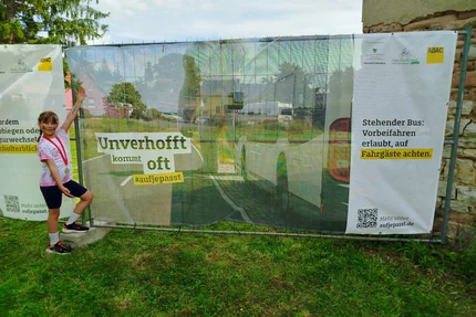 Erxleben © MID Kind neben aufjepasst-Banner „Unverhofft kommt oft“ in Erxleben macht auf Sicherheit an haltenden Bussen aufmerksam.