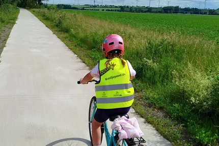 Erxleben © MID Kind auf Fahrrad mit aufjepasst-Warnweste fährt auf ländlichem Radweg vor Feldern und Windrädern.