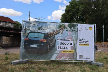 Kampagnenbanner mit einem Auto und einer Giraffe, das auf den Schulterblick vor dem Abbiegen oder Spurwechsel aufmerksam macht.
