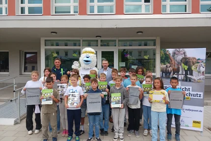 Calbe Saale © AGFK LSA Schulklasse in Calbe mit Kampagnenheften und Turnbeuteln, begleitet vom weißen aufjepasst-Maskottchen.