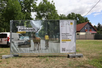 Kampagnenbanner mit Radfahrer und Hirsch, das den seitlichen Mindestabstand von 1,5 Metern beim Überholen innerorts veranschaulicht.
