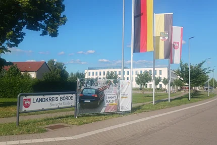 Landkreis Börde © AGFK LSA aufjepasst-Banner mit Giraffenmotiv vor dem Landkreis Börde wirbt für Schulterblick beim Spurwechsel.